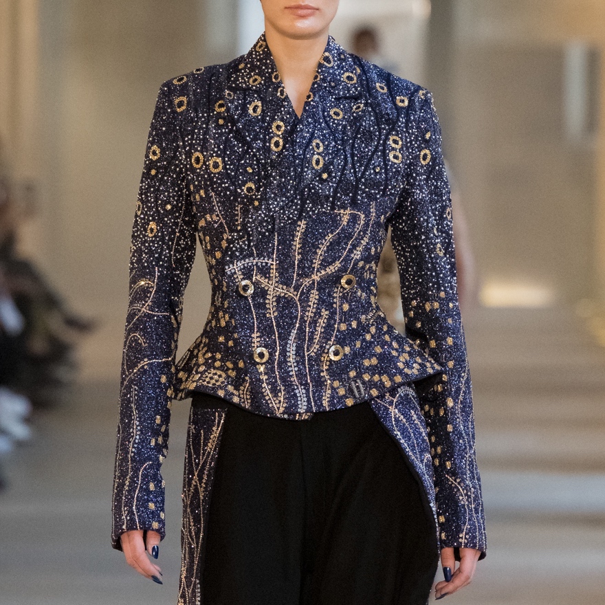 Closeup of a runway model showing an embellished, couture, peplum jacket with matching pants