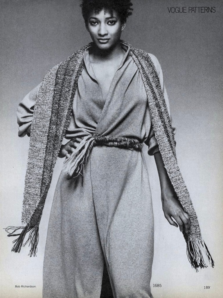 Black and white Vogue editorial photo of a Black model in a wrap dress accessorized with a textured scarf and belt