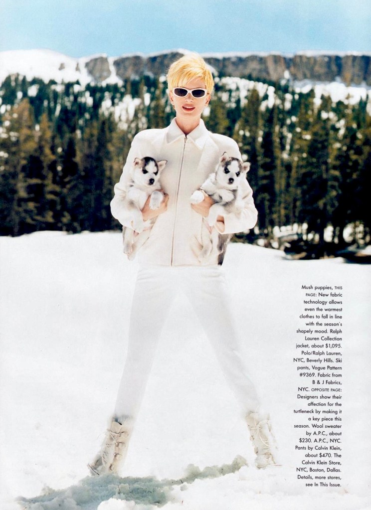 Colour photo of a model standing on a ski slope holding two husky puppies