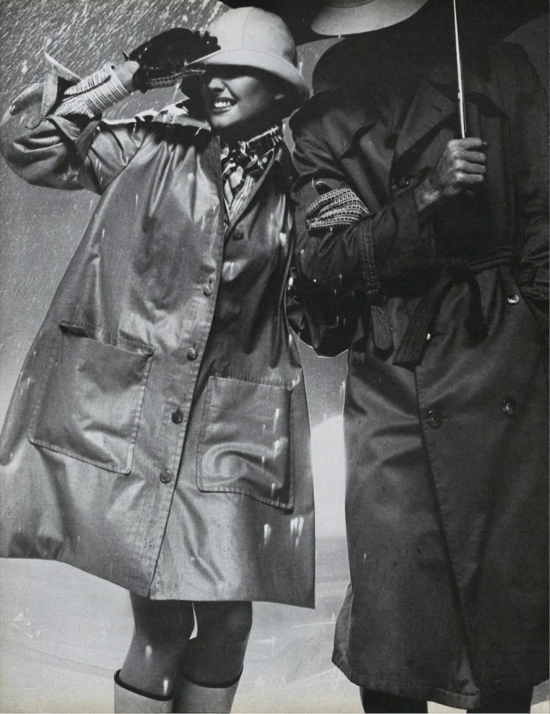Black and white photo of a model caught in the rain, wearing a trapeze-style raincoat (Vogue 2814 by Yves Saint Laurent), hat, gloves, and knee boots, holding the arm of a man holding an umbrella